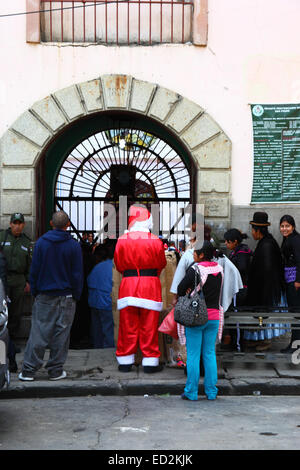 La Paz, Bolivie, le 24 décembre 2014. Le Père Noël attend avec d'autres visiteurs à l'extérieur de la tristement célèbre prison de San Pedro. Tous les visiteurs doivent avoir leurs sacs fouillés avant d'entrer pour visiter les membres de la famille à l'intérieur de la prison. De nombreux enfants accompagner leurs parents condamnés à l'intérieur des prisons en Bolivie car il y a souvent pas d'autre endroit pour eux de vivre ; les organisations sociales prennent souvent présente pour les prisons du pays pour eux à l'époque de Noël. Credit : James Brunker / Alamy Live News Banque D'Images