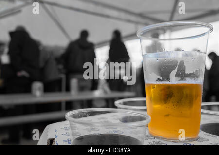 Plastique verre à moitié plein (ou à moitié vide) de bière sur une table (entourée de verres vides) dans une tente. Banque D'Images