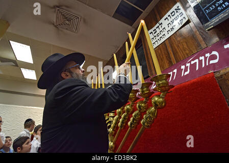 Un rabbin juif orthodoxe s'allume les bougies de Hanoukka étudiant comme congrégation watch contre une synagogue de Brooklyn, NY Banque D'Images