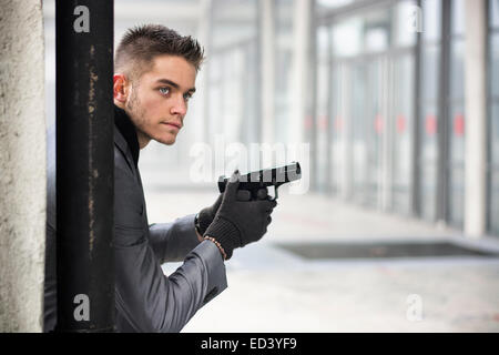 Bien habillé beau jeune détective ou policier ou gangster debout dans un environnement urbain tenant un pistolet avec un déterminé e Banque D'Images
