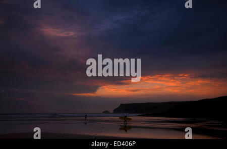 Deux surfeurs de quitter la mer sous un ciel coucher de soleil spectaculaire à Cornwall, Angleterre Banque D'Images