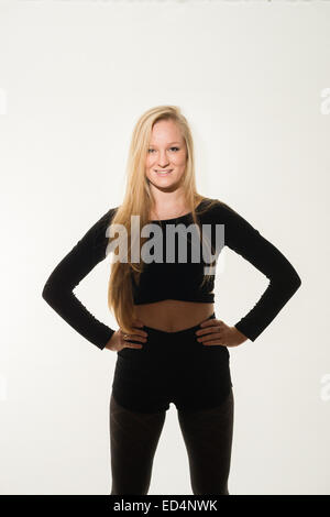 Une happy smiling confident young woman (fille de 18 ans) avec de longs cheveux blonds debout face à l'avance les mains sur les hanches vêtu de noir sur un fond blanc. Banque D'Images