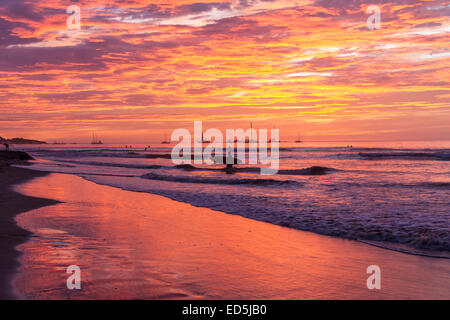 Un surfeur silhouetté contre un coucher de soleil aux couleurs vives comme il arrive avec sa planche de surf à Playa Tamarindo, Costa Rica Banque D'Images