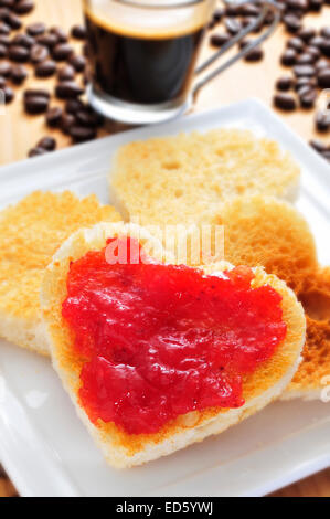 Une plaque en forme de cœur avec des toasts avec de la confiture de fraise avec une tasse de café et grains de café dans l'arrière-plan Banque D'Images