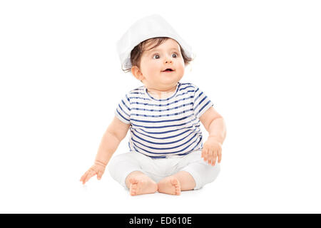 Cute baby girl en tenue de marin assis sur le plancher isolé sur fond blanc Banque D'Images
