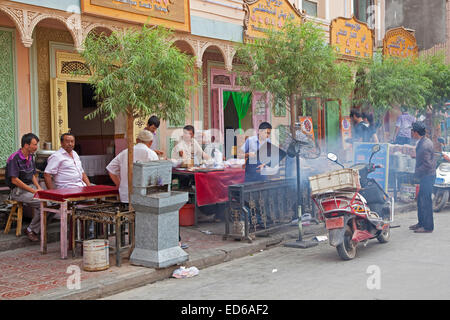 Les hommes de manger de la viande grillée ouïghour en plein air au petit restaurant traditionnel de la ville Kashgar / Kashi, la Province du Xinjiang, Chine Banque D'Images