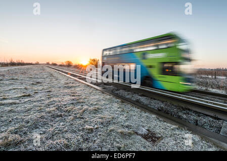 Longstanton près de Cambridge, Royaume-Uni. 30 Décembre, 2014. Météo britannique. Un bus guidé tous les navetteurs à et à partir de la Cambridge sur un gel mais crisp matin au lever du soleil. La température a chuté à moins 1 degrés Celsius la nuit avec un ciel clair, ce qui porte une belle crisp l'aube. Le bus est le plus long du monde dans sa catégorie et s'exécute entre St Ives et Cambridge. Julian crédit Eales/Alamy Live News Banque D'Images