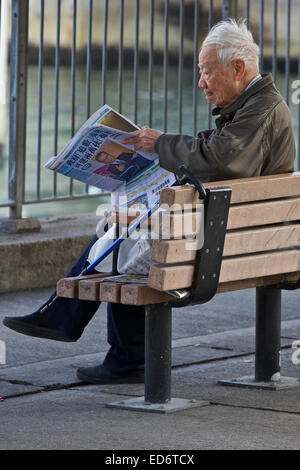 Personnes âgées Chinese Man se lit le journal du matin sur le bord de North Point, Hong Kong. Banque D'Images