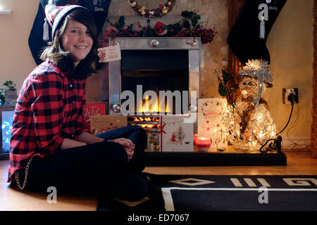 Douze ans smiling girl sitting in front of cheminée décorative à Noël Banque D'Images