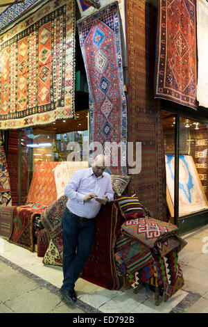 Shopkeeper using smartphone à tapis turc tapis boutique dans le Grand Bazar, Kapalicarsi, grand marché, Beyazi, Istanbul, Turquie Banque D'Images