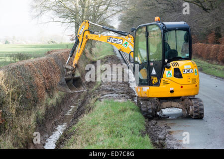 Le nettoyage des fossés de drainage en bordure de route qui avait été envahi par l'utilisation d'un JCB digger. Banque D'Images