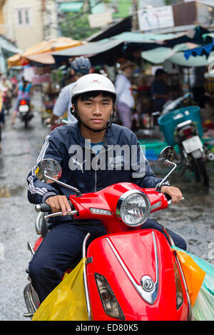 Jeune homme vietnamien sur scooter à travers un marché à Ho Chi Minh Ville. Banque D'Images