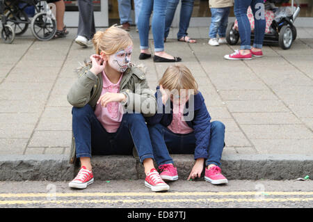 Les jeunes filles avec des visages peints assis sur la chaussée à la Festival International de Marionnettes en Witham, Essex Banque D'Images