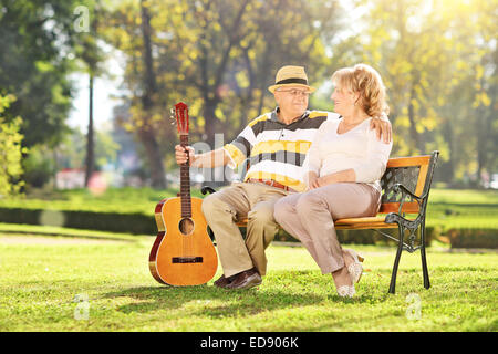Homme mûr assis avec sa femme dans le parc et tenant une guitare Banque D'Images