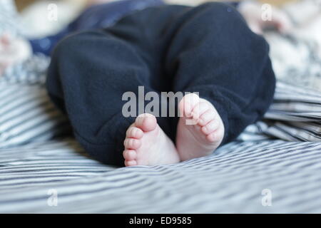 Pieds de bébé sur un lit avec des draps à rayures Banque D'Images