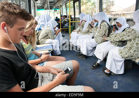 L'école de filles et deux balinais enfants de l'ouest avec leurs téléphones intelligents et les ipod sur un bus à Bali, Indonésie. Banque D'Images