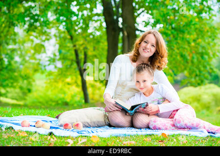 Maman et sa fille dans le parc de la lecture d'un livre Banque D'Images