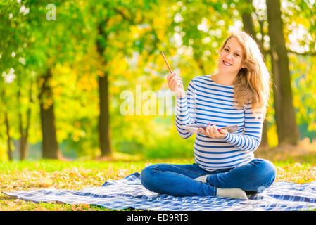 Cheerful pregnant woman avec un ordinateur portable et crayon Banque D'Images