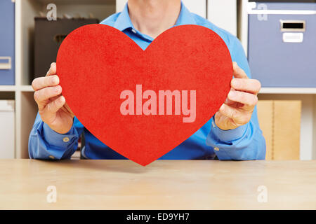 Homme amoureux holding big red Heart in office sur son bureau Banque D'Images