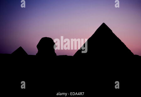 Le grand sphinx et deux des trois anciennes pyramides de Gizeh à la périphérie du Caire, Égypte, se profilent au coucher du soleil. Banque D'Images