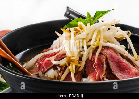 Pho - soupe de nouilles Boeuf rares vietnamiens sur fond blanc avec la sauce hoisin, la sauce piquante, épices, germes, et de basilic frais Banque D'Images