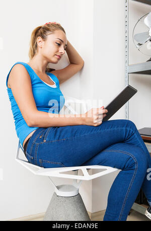 Belle jeune femme est assise sur une chaise à l'aide d'un ordinateur tablette ou ipad Banque D'Images