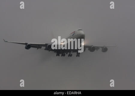 3 janvier 2015, l'aéroport de Heathrow, Londres. Les nuages bas et la pluie fournissent des conditions idéales pour observer service et 'vortex' débourrage comme humidité se condense sur les ailes d'avion à l'atterrissage. Avec la piste visible uniquement à la dernière minute, plusieurs avions ont dû effectuer une 'go-round', abandonnant leurs premières tentatives à la terre. Sur la photo : UN British Airways Boeing 747 jumbo jet se dégage de l'nuages bas instants avant le toucher des roues sur la piste d'Heathrow 27L. Banque D'Images