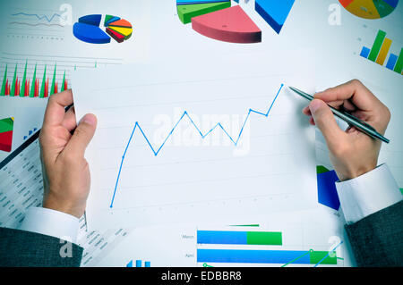 Businessman dans son bureau bureau plein de graphiques et tableaux l'observation d'un graphique avec une tendance à la hausse Banque D'Images
