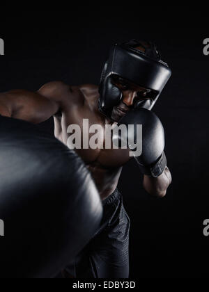 Portrait d'un jeune homme boxer de jeter un coup à l'appareil photo tout en pratiquant sur fond noir. Le port de gant de boxe athlète masculin Banque D'Images