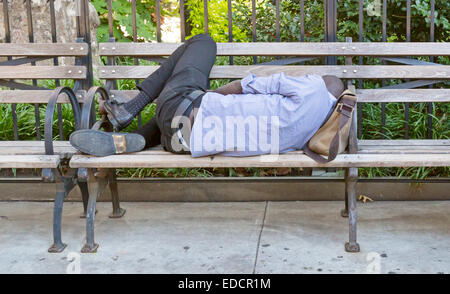 Un homme dort sur un banc de parc de la ville. Banque D'Images