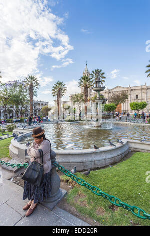 Femme en costume traditionnel et un chapeau en appui sur une fontaine à la Plaza de Armas, Arequipa, Pérou Banque D'Images