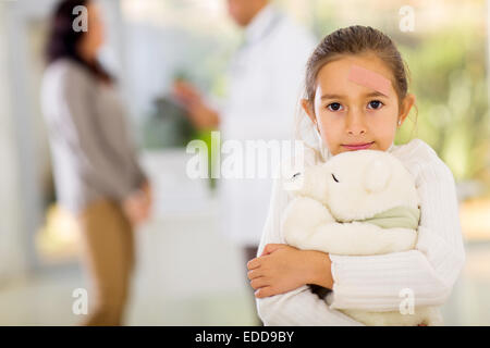 Fille mignonne avec cataplasme sur son visage holding a teddy bear en bureau de médecins Banque D'Images