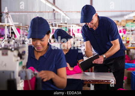 Usine de confection sourire foreman expliquer les travaux d'young machiniste Banque D'Images