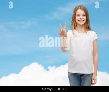 Petite fille en blanc T-shirt montrant le geste de paix Banque D'Images