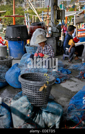 Inversion des rôles avec l'homme s'occuper de bébé tout en femme tend les filets de pêche. Thaïlande S. E. l'Asie. Banque D'Images
