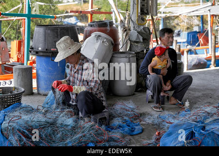 Inversion des rôles avec l'homme s'occuper de bébé tout en femme tend les filets de pêche. Thaïlande S. E. l'Asie. Banque D'Images