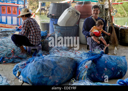 Inversion des rôles avec l'homme s'occuper de bébé tout en femme tend les filets de pêche. Thaïlande S. E. l'Asie. Banque D'Images