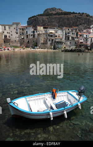 Un petit bateau de pêche amarré dans le vieux port de Cefalu Sicile Italie avec de vieux bâtiments dans la vieille ville à l'arrière-plan. Banque D'Images