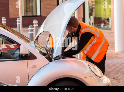 Mécanicien d'hommes travaillant sur une voiture avec le capot avant (capot). Il porte une veste hi-viz orange. Concept qui dérange. Banque D'Images