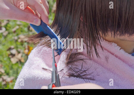 Close up of a young woman combing et couper la longue chevelure sombre, humide, d'un jeune homme à l'extérieur dans l'herbe sur une journée ensoleillée d'automne Banque D'Images