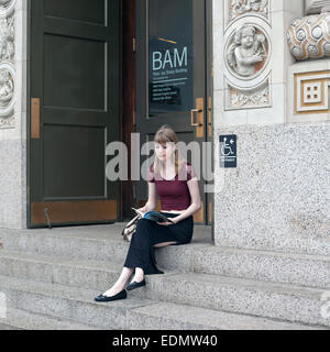Une femme se lit sur les marches de la Brooklyn Academy of Music de New York. Banque D'Images