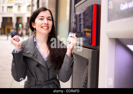 Jeune femme célébrations aux cash machine Banque D'Images