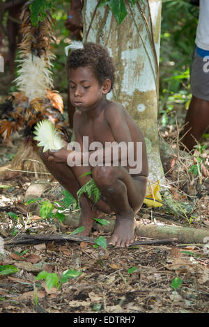 La Mélanésie, Vanuatu, Rano Island. Village garçon dans l'habitat forestier de vêtements autochtones souffle feuille de palmier. Banque D'Images