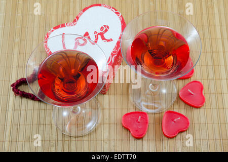 Deux verres d'une boisson alcoolique rouge en forme de cœur et des bougies sur une table de bambou Banque D'Images