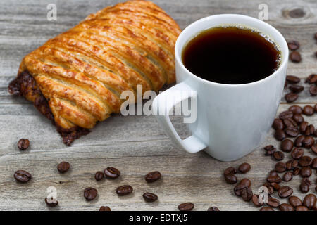 Gros plan d'une tasse de café noir, grand pain au chocolat et des grains torréfiés sur fond de bois rustique. Banque D'Images