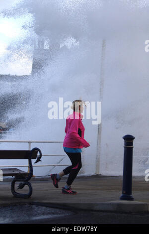 Aberystwyth, Pays de Galles, Royaume-Uni. 10 janvier, 2015. Météo britannique. Un jogger est prise par l'un des énormes vagues fracassant dans la digue à Aberystwyth que les tempêtes a frappé le Royaume-Uni Crédit : Jon Freeman/Alamy Live News Banque D'Images