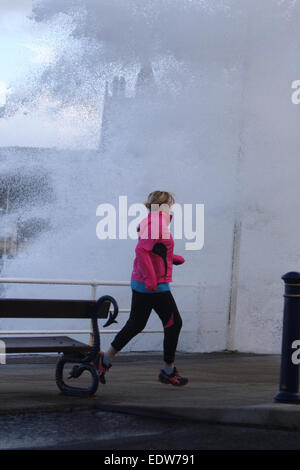 Aberystwyth, Pays de Galles, Royaume-Uni. 10 janvier, 2015. Météo britannique. Un jogger est prise par l'un des énormes vagues fracassant dans la digue à Aberystwyth que les tempêtes a frappé le Royaume-Uni Crédit : Jon Freeman/Alamy Live News Banque D'Images