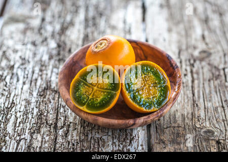 Couper vert vif et orange fleshed naranjilla dans un bol en bois sur table en bois rustique Banque D'Images