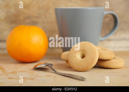 Une pile de cookies ronde près d'une tasse de lait et une orange sur une table en bois Banque D'Images