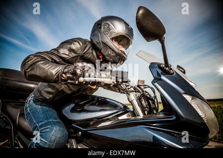 Biker dans casque et blouson de cuir racing sur la route Banque D'Images